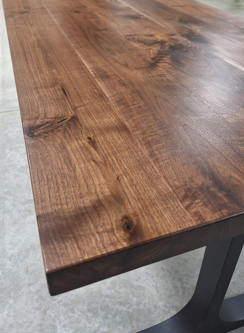 Corner of a solid walnut dining table top on a black metal base