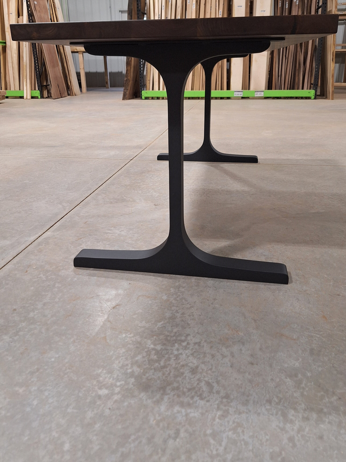 Side view of the black metal T-base under a walnut dining table