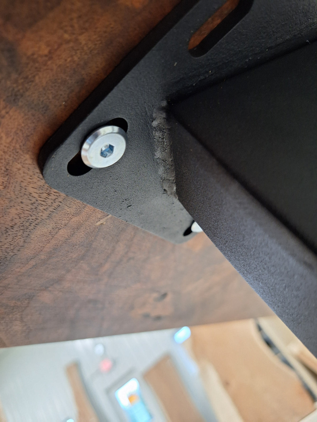 Underside of a walnut table showing the metal leg mounting hardware