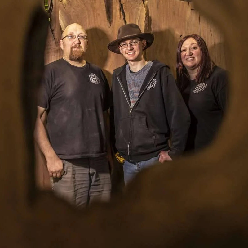 Three members of the Knot Just Lumber team standing, viewed through a knot hole
